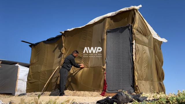 النازح الفلسطيني عماد أبو زيد يقوم بتمتين خياطة خامات المظلات التي تلقى بها المساعدات من الجو للنازحين في قطاع غزة والتي صنع منها خيمة تأويه وعائلته المكونة من 10 أشخاص (14 أبريل نيسان 2024)